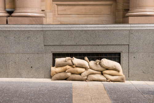 Sandbags along the footpath lining the lower windows of a building in Brisbane CBD before a cyclone - Australian Stock Image
