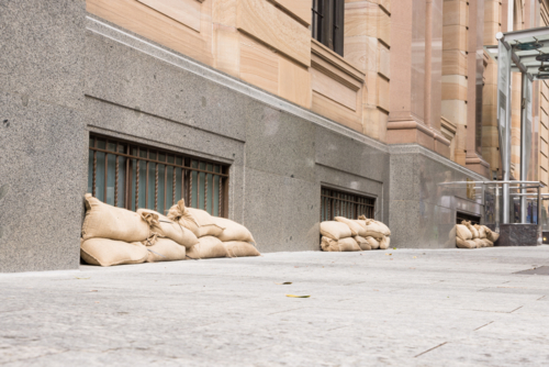 Sandbags along the footpath lining the lower windows of a building in Brisbane CBD before a cyclone - Australian Stock Image