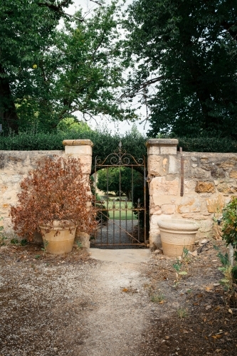 Sandstone wall with iron gate leading to green garden - Australian Stock Image