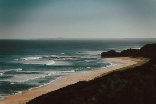 Sandy beach with gentle waves and rocky cliffs - Australian Stock Image