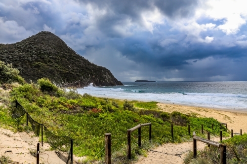 Sandy track leading to beach against mountain and cloudy sky - Australian Stock Image