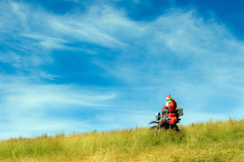 Santa Claus riding a motorbike through a grassy paddock under a bright summer sky - Australian Stock Image