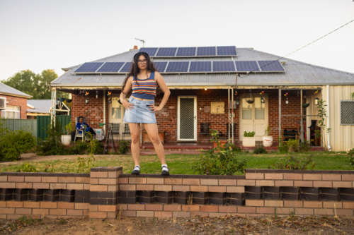 sassy teenager with headphones wearing short denim skirt standing on low wall in front of older home - Australian Stock Image