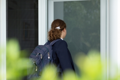 School girl arriving home from school seen from behind bushes