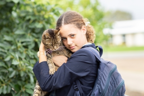 Schoolgirl cuddling tabby cat - Australian Stock Image