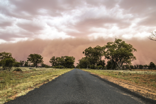 Sealed road stretching into the distance with dust cloud storm in the sky - Australian Stock Image
