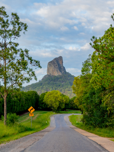 Sealed road through green bushland leading to mountain peak in background - Australian Stock Image