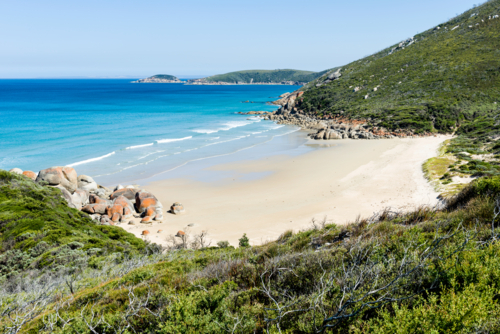 Secluded beach with orange-tinted boulders and clear blue water - Australian Stock Image