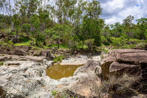 Secluded natural waterhole among rugged exposed rock formations and eucalyptus bushland - Australian Stock Image
