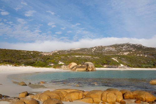 secluded white sand beach with rocks in foreground - Australian Stock Image