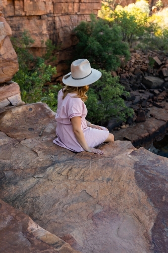 seen from behind young woman sitting on rock ledge in East Kimberley - Australian Stock Image