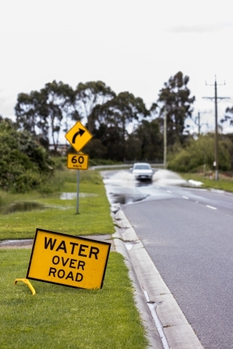 selective focus on a 'water over road' sign with an out of focus unrecognisable car in background - Australian Stock Image