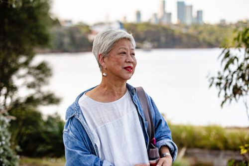 Senior Asian woman standing along the waterfront - Australian Stock Image