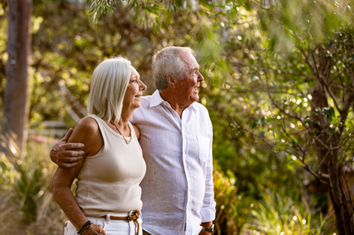 Senior couple walking in public park with arm wrapped around the other - Australian Stock Image