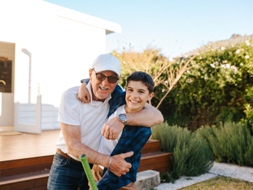 Senior guy hugging a young boy outside the house. - Australian Stock Image