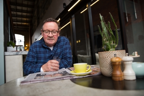 Senior Man Drinking Coffee and Reading Newspaper - Australian Stock Image