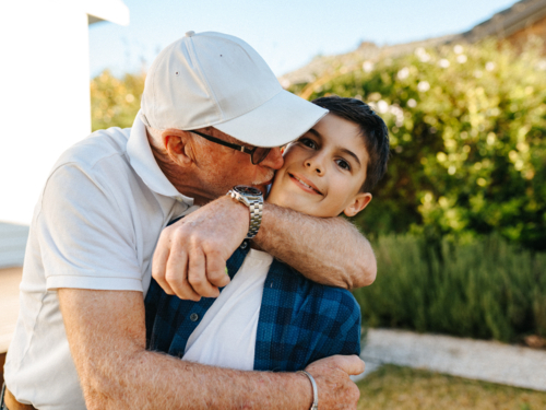 Senior man kissing his grandson on the cheek. - Australian Stock Image