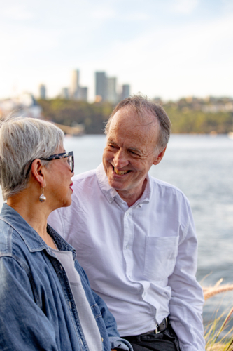 Senior man looking at Asian woman while sitting outdoors near the water - Australian Stock Image