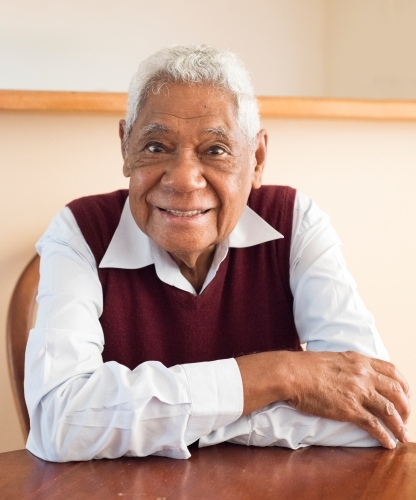 Senior man with Indonesian heritage smiles in profile photo while sitting indoors. - Australian Stock Image