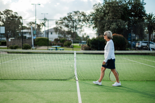 Senior woman in sports attire strolls along the tennis court - Australian Stock Image