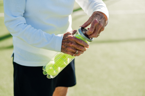 Senior woman prepares for tennis by opening a canister of bright yellow balls outdoors - Australian Stock Image