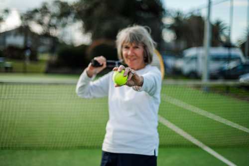 Senior woman prepares to serve a tennis ball during a match at an outdoor court - Australian Stock Image