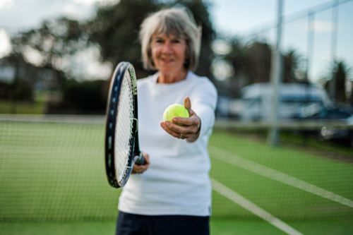 Senior woman prepares to serve a tennis ball on an outdoor court - Australian Stock Image
