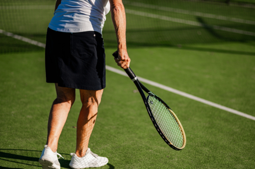 Senior woman prepares to serve on a tennis court - Australian Stock Image
