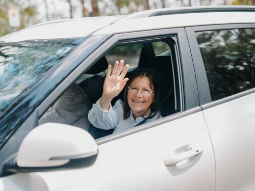 senior woman smiling waving out of car window - Australian Stock Image