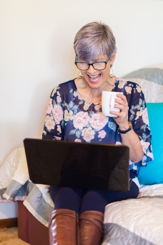senior woman working on laptop on lounge with a cup of tea - Australian Stock Image
