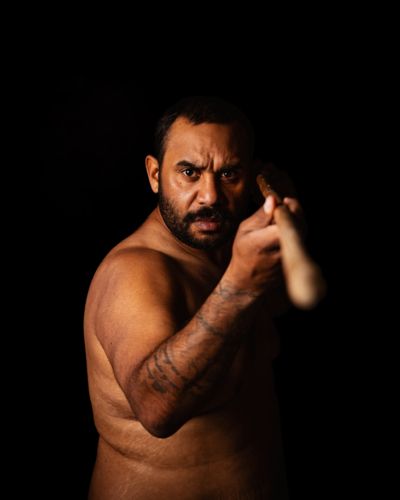 Serious Aboriginal male holding spear out with eye contact - Australian Stock Image