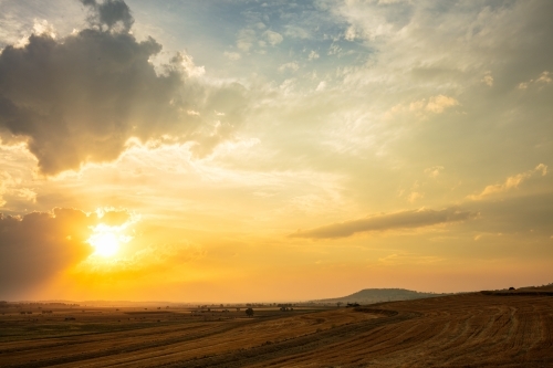 Setting yellow sun through cloud over a rural area of Queensland - Australian Stock Image