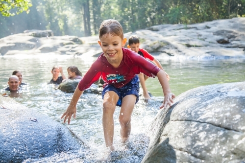 Seven year old boy splashing in river water between two rocks - Australian Stock Image