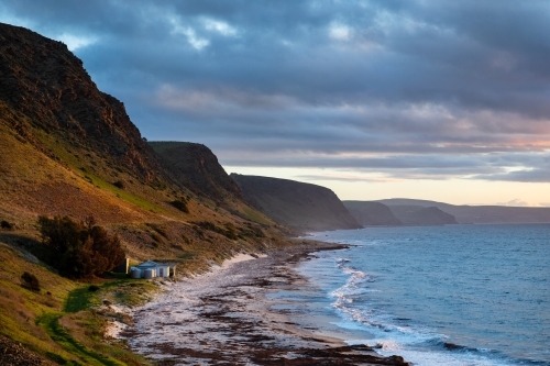 shack on beach at base of steep hill - Australian Stock Image
