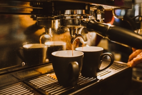 Shots of coffee dripping from machine into cups - Australian Stock Image