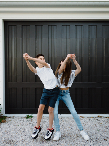 Siblings bumping hips outside in their yard. - Australian Stock Image