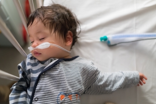 Sick mixed race year old boy asleep being treated with oxygen therapy in Children's Hospital ward - Australian Stock Image