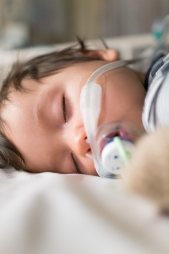 Sick mixed race year old boy asleep being treated with oxygen therapy in Children's Hospital ward - Australian Stock Image
