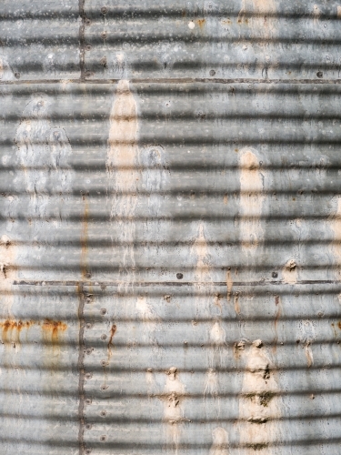 Side of an old, leaky corrugated iron water tank