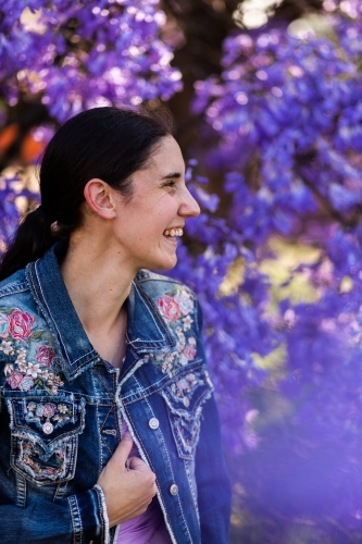 Side on profile of happy woman laughing in spring with background of purple jacaranda flowers - Australian Stock Image