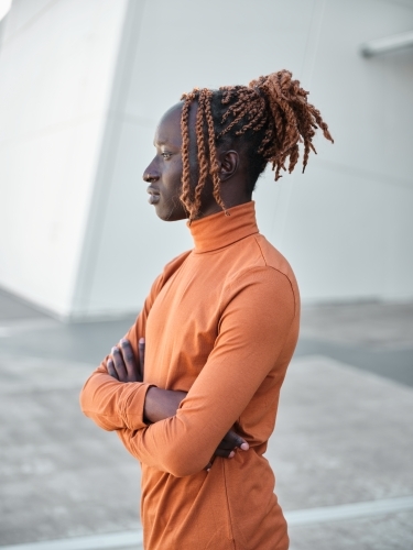 Side profile of South Sudanese man wearing orange turtleneck with arms folded