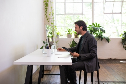 Side view of a happy business man working at a desk in a studio space - Australian Stock Image