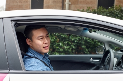 Side view of Asian man driving in car looking out window - Australian Stock Image