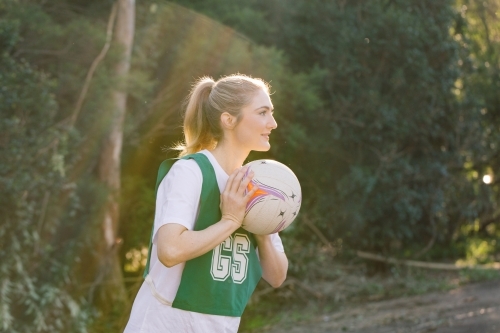 side view shot of a young woman in sports wear holding a net ball with two hands on a sunny day - Australian Stock Image