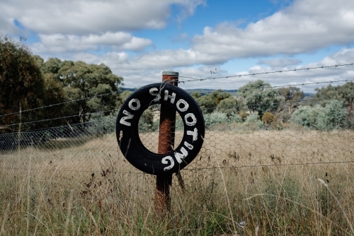 Sign made from old black tyre tied to a rusted post with a white painted message "NO SHOOTING"