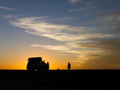 Silhouette against the sunset of a 4WD and people