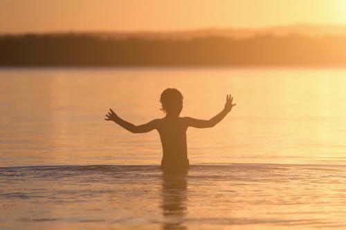 Silhouette of a child in water at sunset