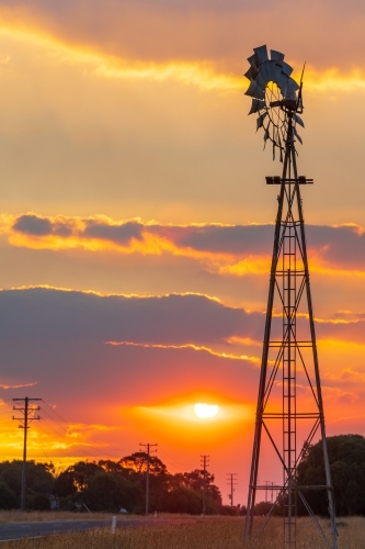 Silhouette of a farm windmill against a smokey sunset sky - Australian Stock Image
