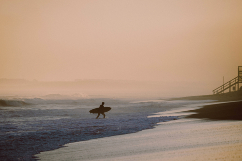 Silhouette of a lone surfer getting off the beach with his board - Australian Stock Image