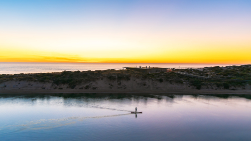 Silhouette of a man paddle boarding along the Onkaparinga River at dusk in South Port - Australian Stock Image